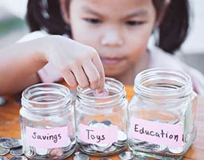 Young girl putting money in savings jars.
